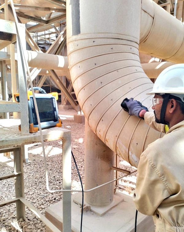 Inspector testing pipework with portable NDT equipment